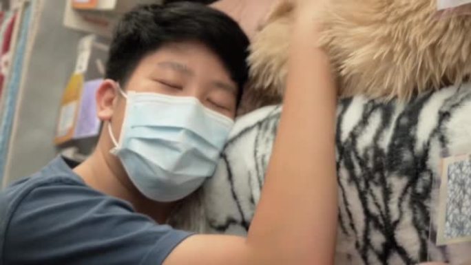 亚洲少年男孩戴着口罩触摸地毯挂在家具店与家人在一起，购物生活方式的概念。