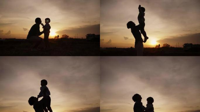 快乐的家庭亚洲爸爸和男婴在剪影日落的夏天一起在户外玩耍。