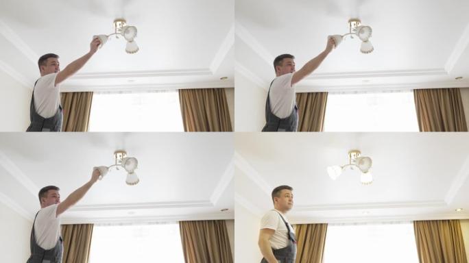 一名男电工更换顶灯中的灯泡。