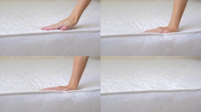 一个女孩的手的特写检查一个新的舒适的矫形白色床垫的刚度。女性手压在矫形表面。女孩测试弹性柔软矫形床垫