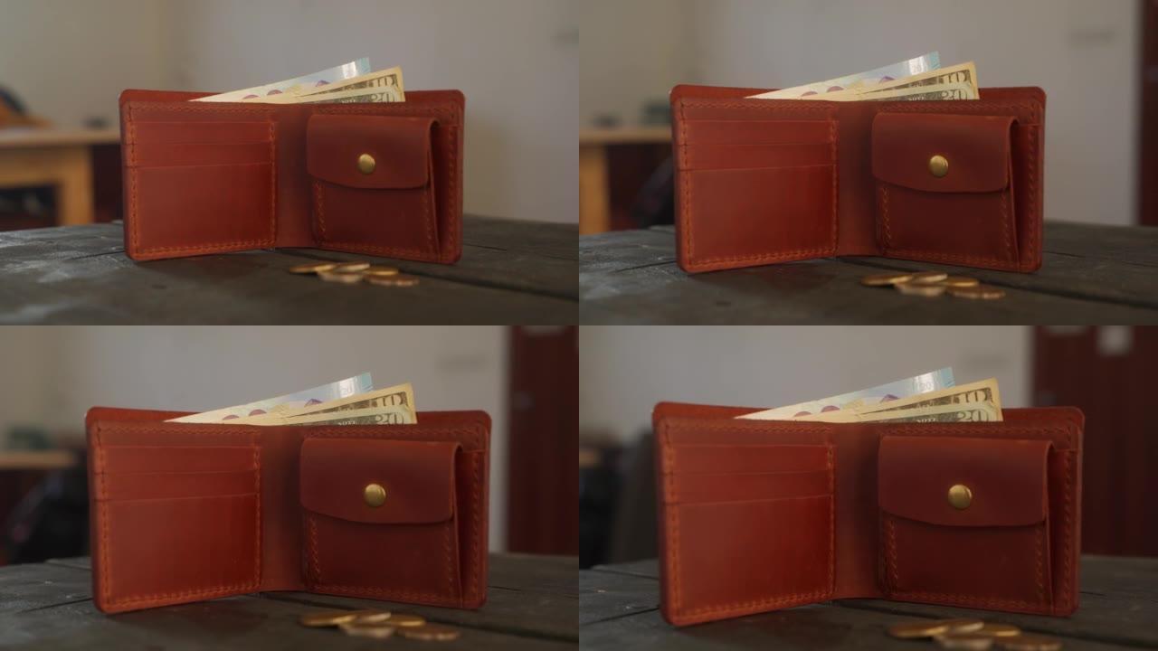 棕色双折钱包，带硬币袋、持卡人和现金，放在皮革车间的深色木制桌子上。小袋，钱，美元和欧元纸币，带有复