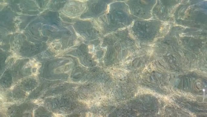 太阳的眩光反映在最纯净的透明海水特写，沙质海底。由于微风，小浪冲入水中
