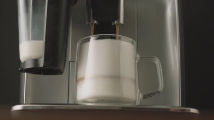 将新鲜酿造的卡布奇诺咖啡从咖啡机中倒入玻璃杯中。