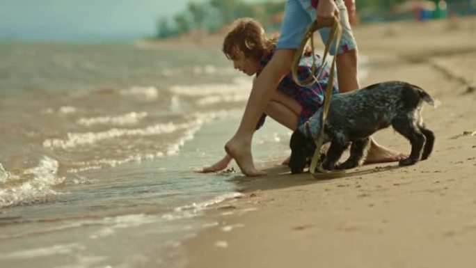 男孩和一个女孩正坐在河边，他们心爱的宠物正坐在岸边。与狗的朋友在河边度过时光，用手触摸海浪。河边节日