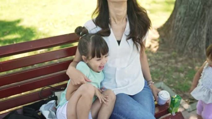 可爱的小女孩和妈妈在公园的长凳上吃早餐