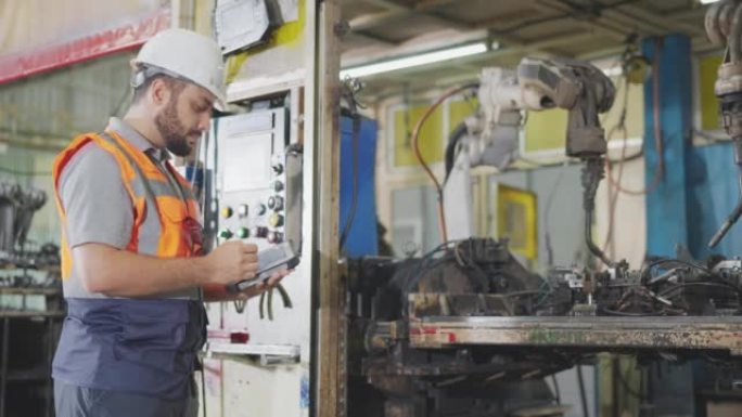 机器人工程师在某工业工厂的机器人面前，用数字平板对焊接装配工艺进行了改进，以减少生产过程中的零件缺陷