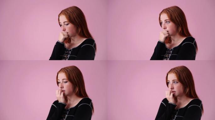 4k视频，一个紧张的女孩在粉红色的背景上咬指甲。
