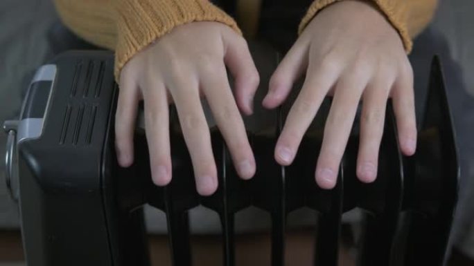 一个十几岁女孩的手放在电散热器上。