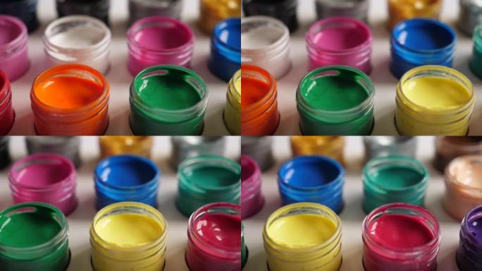 将水粉画颜料放在罐子里明亮的颜色特写。塑料罐上的多色水粉套装。多莉拍摄多色背景。多色油漆的背景。创意