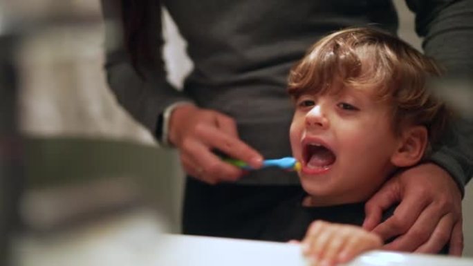 父母用牙刷刷孩子的舌头。母亲清洁孩子的嘴。牙齿卫生概念