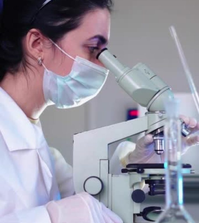 垂直视频，医学实验室的女性微生物学家在显微镜下观察。科学家，使用高科技设备。药学、生物化学、科学概念