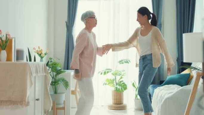 快乐的亚洲家庭，年幼的女儿和退休的资深妈妈跳舞最喜欢的歌曲，周末在家里的客厅里共度时光。
