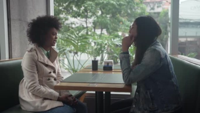 Two young diverse women sitting at coffee shop in 