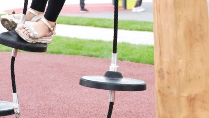 夏季凉鞋中儿童脚的特写镜头克服了绳索公园上的障碍，孩子正在平衡寻找平衡。体育游戏和娱乐，发展