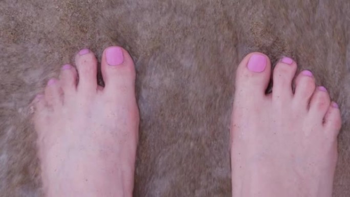 粉红色指甲的女人的腿。海浪和沙卷。从上方观看