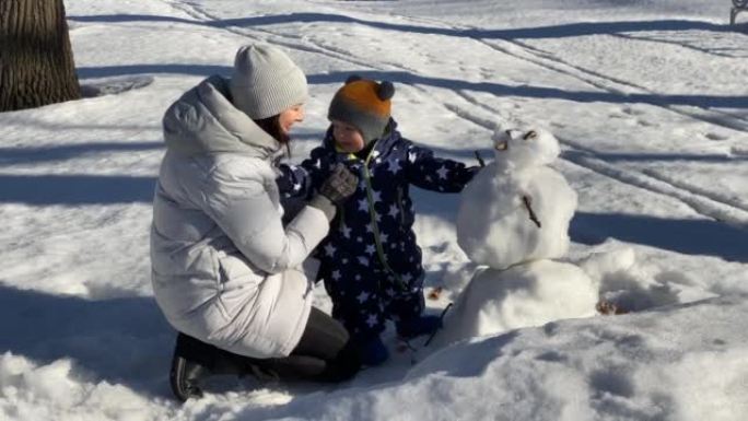 孩子在雪地里迈出了第一步，和妈妈一起散步。1岁的男婴在冬天学习与妈妈在公园散步。