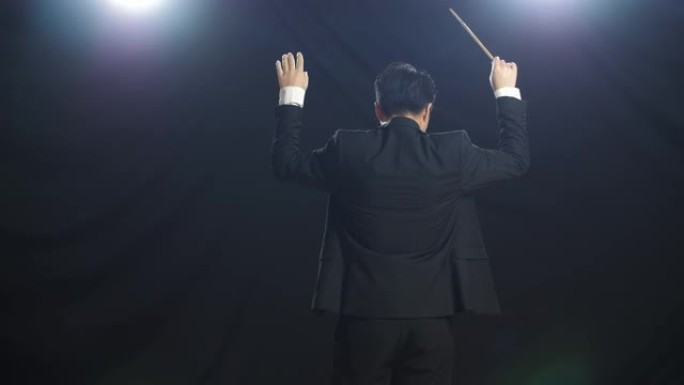 亚洲指挥家男子手持指挥棒在黑色工作室展示手势的背影
