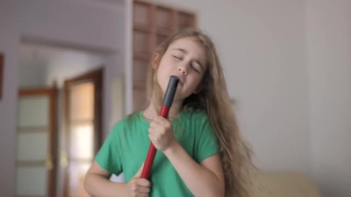 富有创造力的少女唱歌，用扫帚手柄作为麦克风。儿童在家庭房间唱歌时用拖把作为麦克风。享受家庭清洁。顽皮