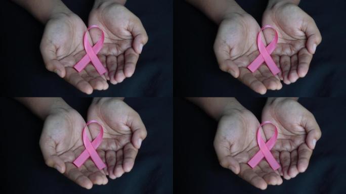 黑色背景手掌上的粉红丝带乳腺癌意识图标徽章。世界癌症日，10月粉红日，全国癌症幸存者日概念。
