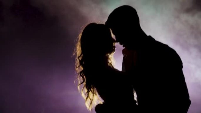 年轻夫妇在烟雾笼罩的黑暗空间中跳舞。慢动作。剪影