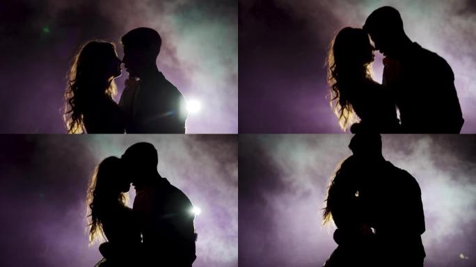 年轻夫妇在烟雾笼罩的黑暗空间中跳舞。慢动作。剪影