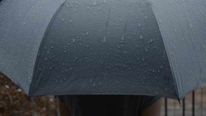 灰色雨伞上的雨。曼谷晚上雨中的银伞。镜头雨滴落在雨伞上。代表恶劣天气冬季雨季或保护。雨中的人和雨伞。