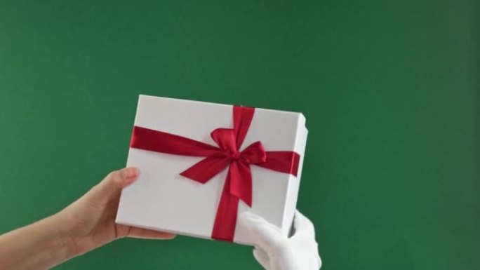 圣诞老人手持礼品盒，红丝带隔离在绿色背景上。特写。圣诞节祝贺。色度键屏幕。冬季礼物。提出产品。广告手