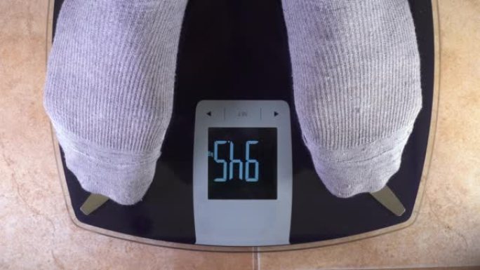 一个穿着灰色棉袜的男人踩在秤上。需要减轻重量的概念。肥胖危险。观点。