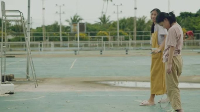 哭泣的亚洲女孩站着不动，而姐姐在室外球场上打羽毛球。生活方式概念。