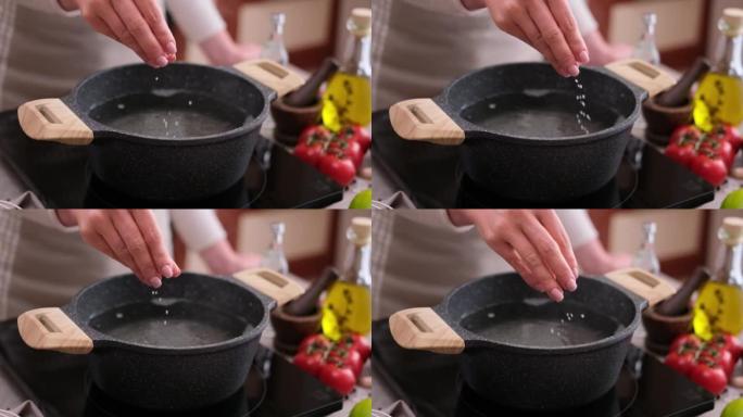 女人在家用厨房的电磁炉上的锅中向沸水中加盐