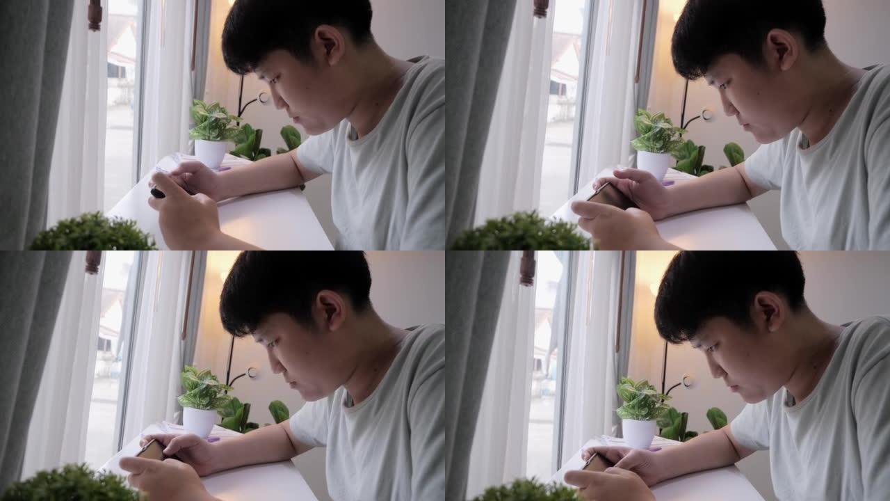 亚洲少年男孩在家玩窗户附近的手机游戏，生活方式概念。