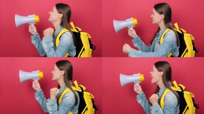 穿着牛仔夹克和黄色背包的肖像年轻女子学生拿着尖叫扩音器宣布折扣销售快点孤立在工作室的红色背景墙上。大