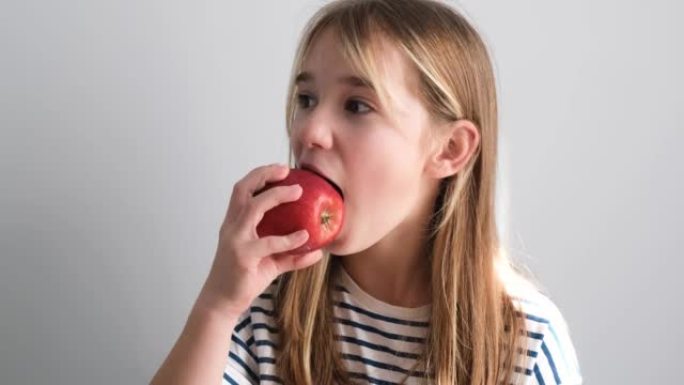 一个小女孩坐在厨房里吃苹果当早餐。美味的红苹果