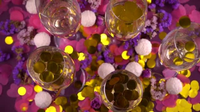 杯中掉落的五彩纸屑配起泡酒，圆形糖果配椰子片，心形五彩纸屑和紫色背景上的花朵。慢动作。