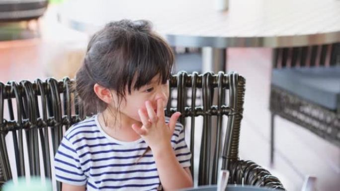 亚洲小女孩在吃东西时流鼻涕和打喷嚏。年轻可爱的小孩坐在餐桌上，生病和生病，在咖啡馆餐厅过敏和打喷嚏。