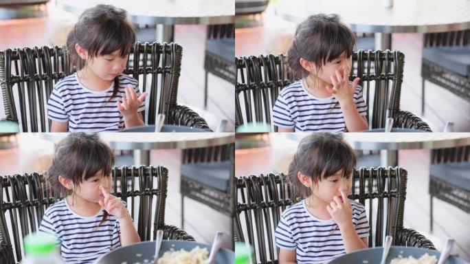 亚洲小女孩在吃东西时流鼻涕和打喷嚏。年轻可爱的小孩坐在餐桌上，生病和生病，在咖啡馆餐厅过敏和打喷嚏。
