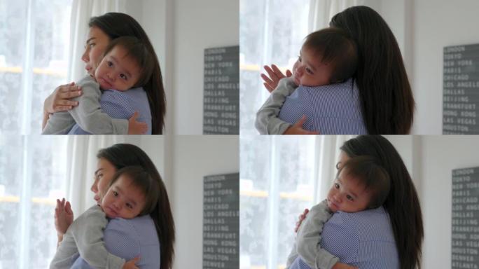 亚洲母亲将婴儿抱在肩膀上，使昏昏欲睡的女儿昏昏欲睡。