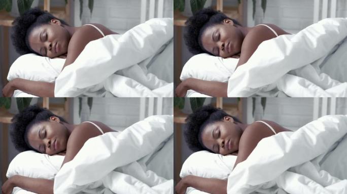 宁静的非洲裔美国妇女睡在舒适的床上，躺在柔软的枕头矫形床垫上醒来，平静的年轻黑人女士躺在卧室的白色床