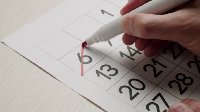 男人的手用红笔在纸质日历上写下第六天。