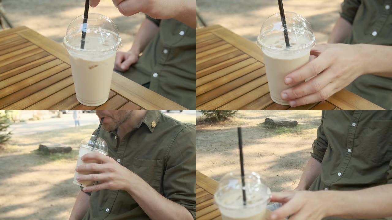 男子在夏季咖啡馆的桌子上的塑料一次性杯子里喝冰拿铁。夏季清凉饮料