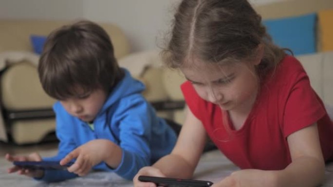 孩子们躺在家里的电话里玩游戏。孩子们在手机上玩视频游戏。男孩和女孩玩电子游戏智能手机。朋友使用手机进