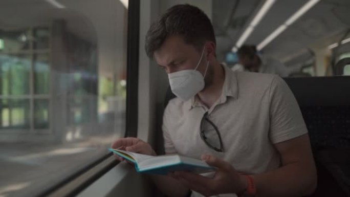 戴着防护口罩的通勤者坐在窗户旁，在穿越德国的火车旅行中看书。一名蒙面火车乘客在巴伐利亚看书。乘火车旅