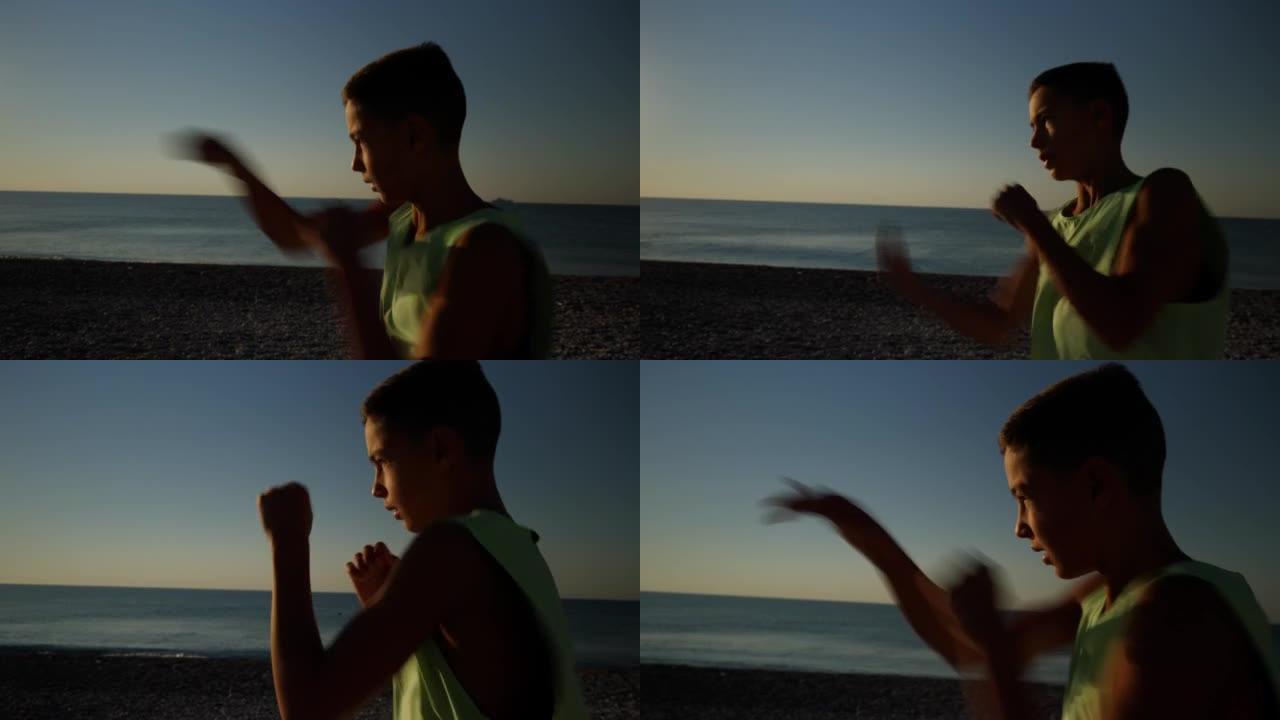 年轻的男拳击手或空手道战士在日出时在海滩上训练。男孩早上做太极拳的剪影镜头。高质量4k镜头