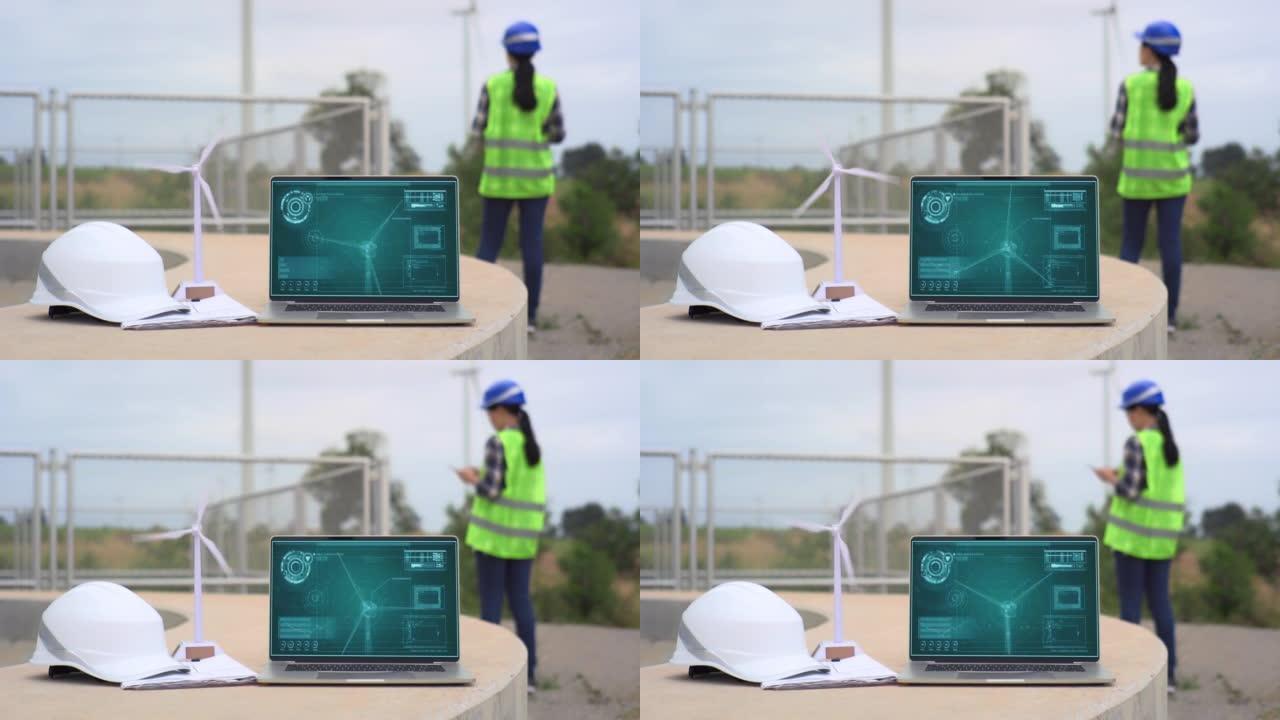 笔记本电脑与未来现实技术的风车显示在桌子和工程师在风力涡轮机农场工作的背景。