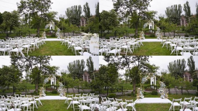 户外婚礼的婚礼装饰品。金色拱门装饰有白色和蓝色的玫瑰，天然花朵。绿色草坪上供客人使用的白色椅子。夏季