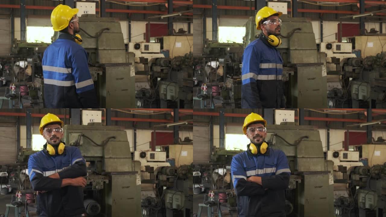 工业工程师回头看着戴着安全镜和带有工厂背景的黄色头盔的相机。