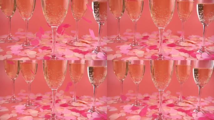 在粉红色的背景上带有起泡酒的杯子，上面带有飘落的五彩纸屑。慢动作。