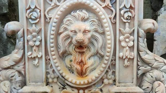古老的白色大理石喷泉装饰着一只喷出水的狮子的头，带有古老纹理的童话中的宫殿装饰品
