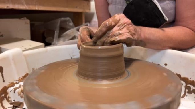 成年中年妇女的手在陶工的电机织机上制作陶杯或杯子，粘土变成了精美的产品艺术和消遣有趣的动作，您可以永