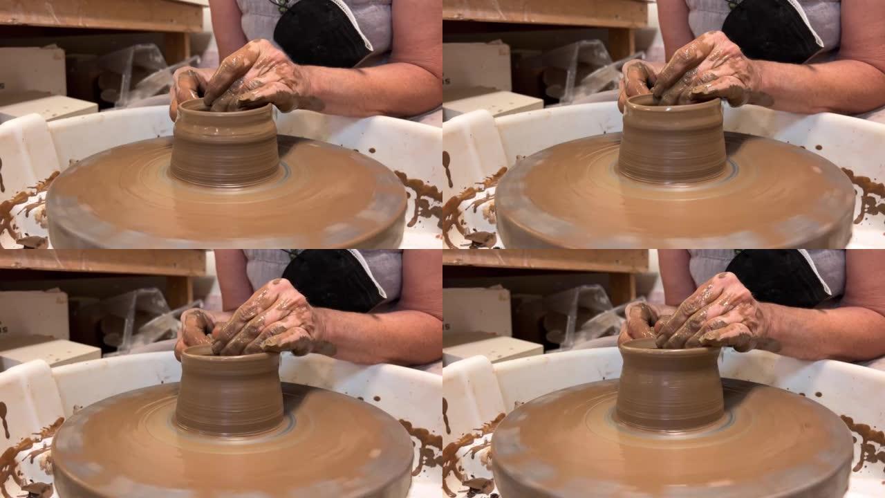 成年中年妇女的手在陶工的电机织机上制作陶杯或杯子，粘土变成了精美的产品艺术和消遣有趣的动作，您可以永